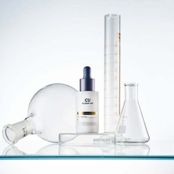 Front view of EX-C RE n Calm Ampoule serum with glass beakers on a reflective surface.