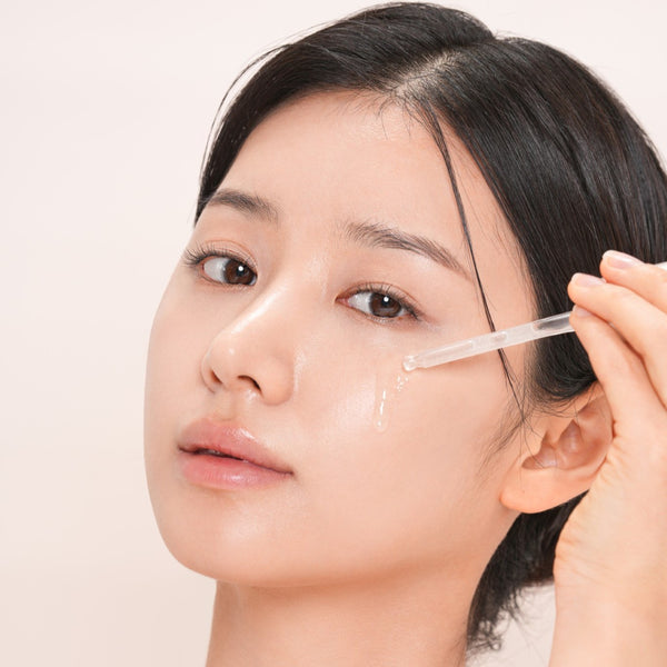 Woman applying a skincare product to her face with a dropper.