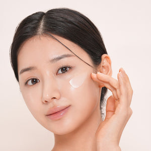 Woman applying dr solution pdrn bakuchiol cream 100 moisturizer to her face with a beige background.
