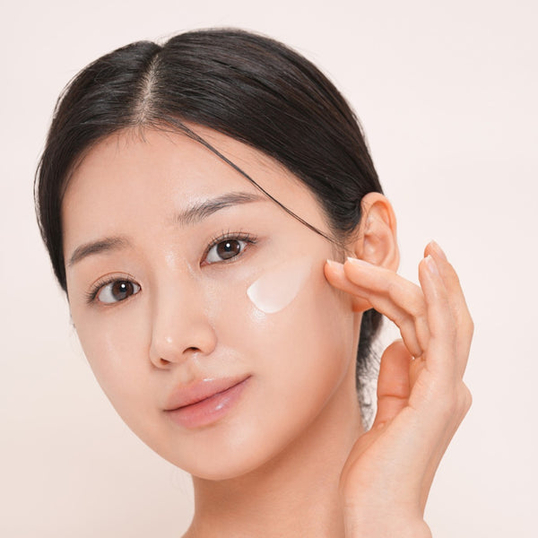 Woman applying dr solution pdrn bakuchiol cream 100 moisturizer to her face with a beige background.