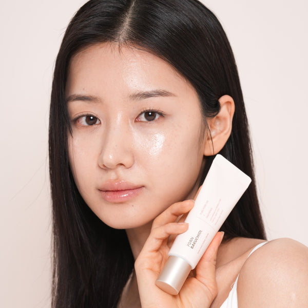 Woman holding dr solution pdrn bakuchiol cream 100 moisturizer with a plain background.